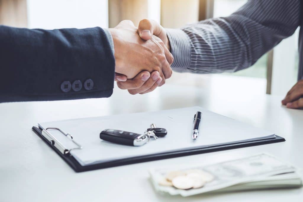 Two men shaking hands after one just purchased a used rental car.