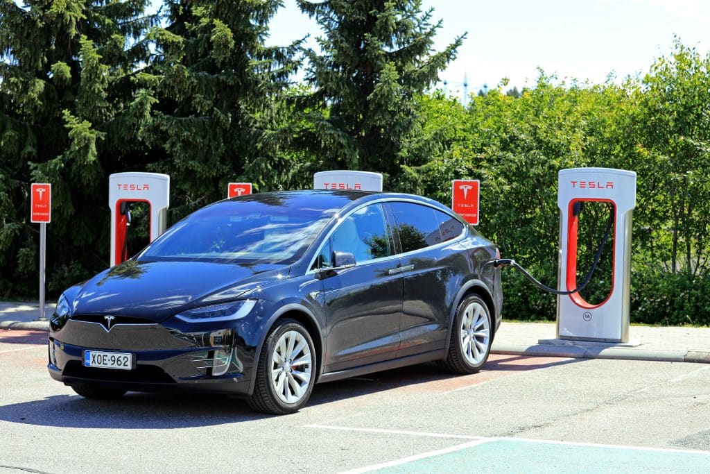 Dark blue Tesla Model X plugged in and charging at a Tesla supercharging station in a parking lot. 