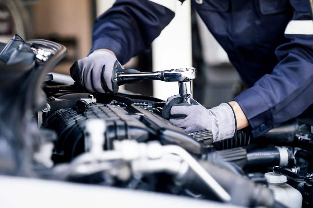 A mechanic working on the engine of a car while wearing gloves.