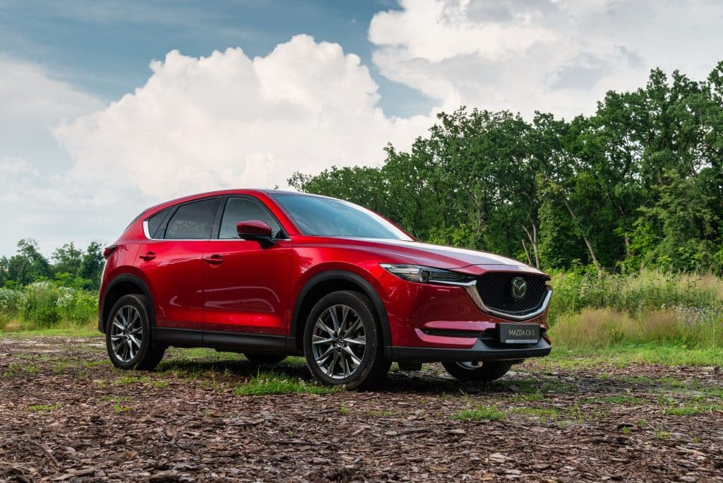 Red 2021 Mazda CX-5 parked on a dirt road in front of a forest. 