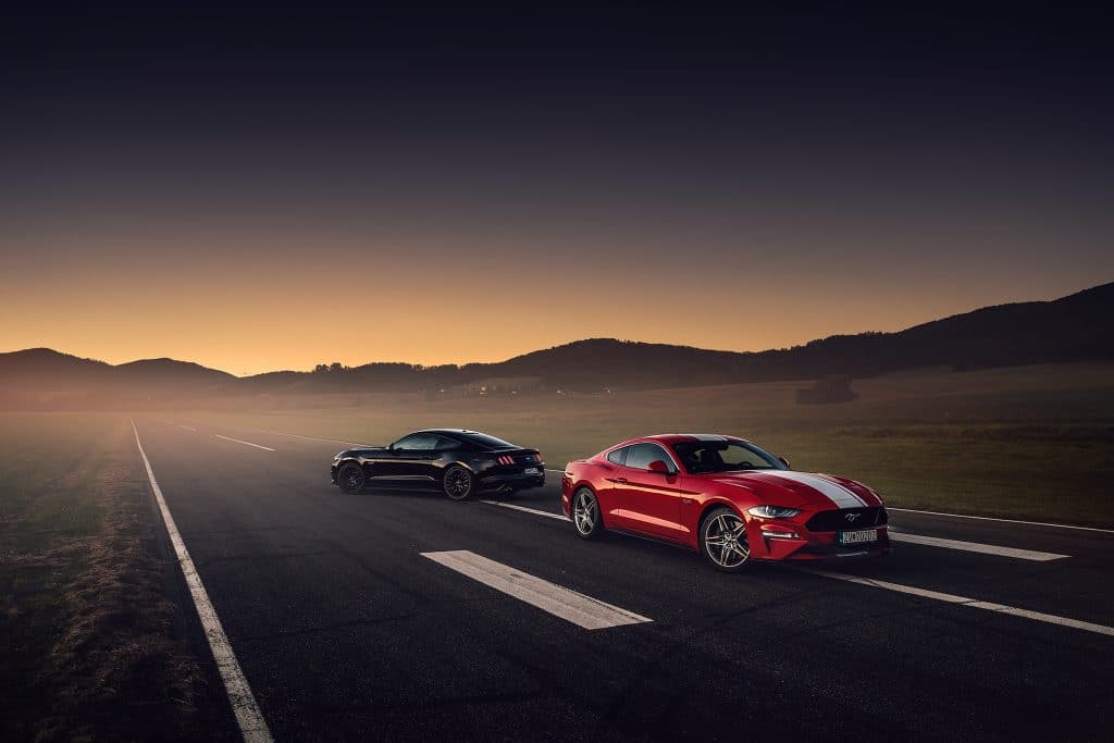 Two 2020 Ford Mustangs parked on a road in front of mountain scenery. 