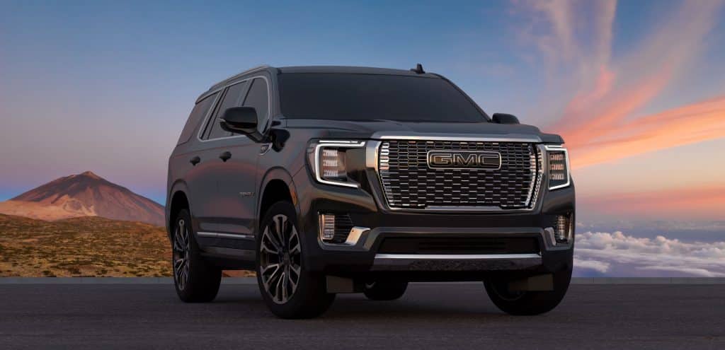 Black GMC Yukon Denali in front of a rainbow-colored sky and mountains.