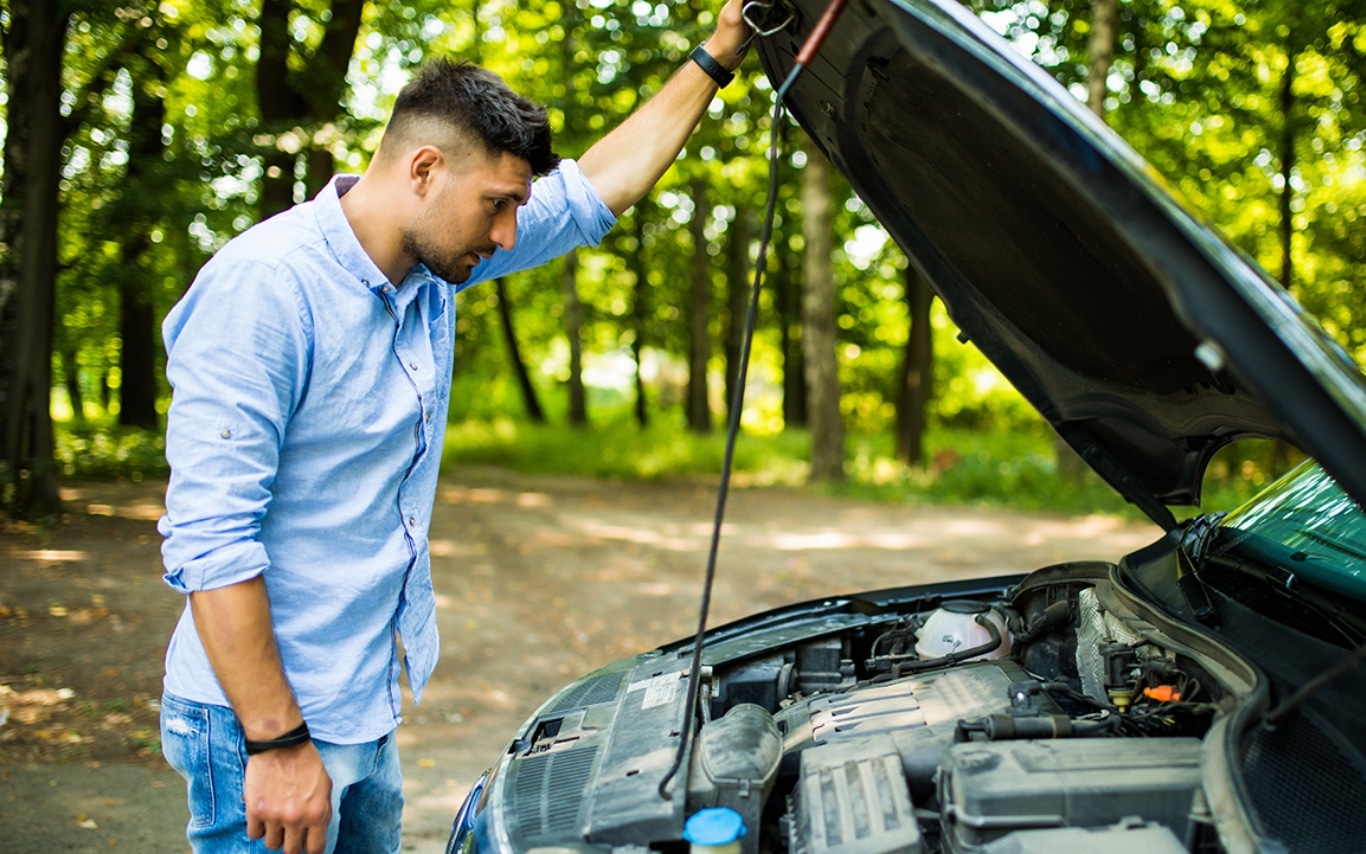 Man standing in front of his car with the hood up, looking down at the engine.