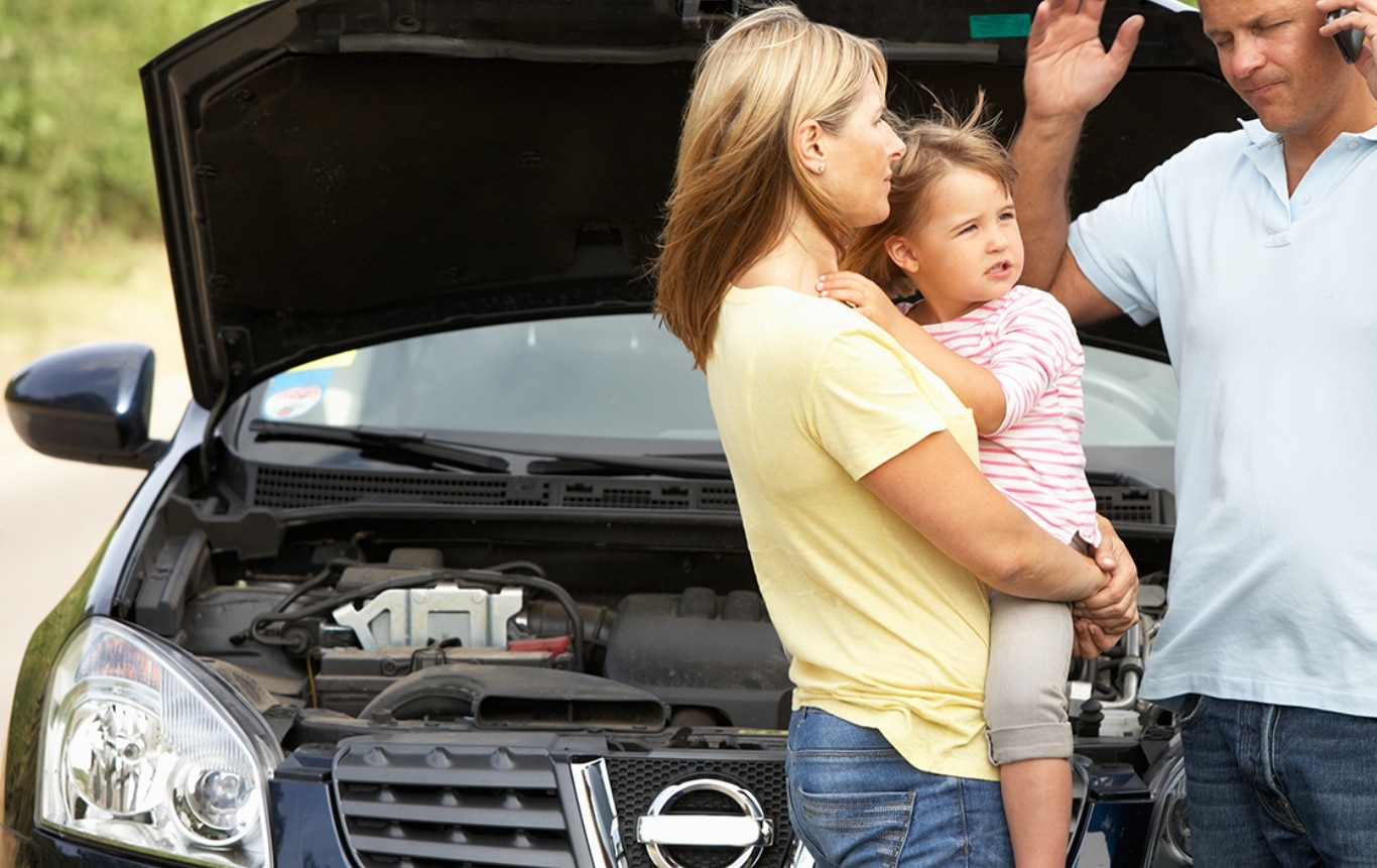 Two parents with their young child, frustrated standing in front of their broken down car with the hood up.