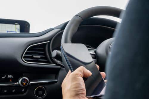 Hand holding an iPhone with a black screen in the driver seat of a car. 