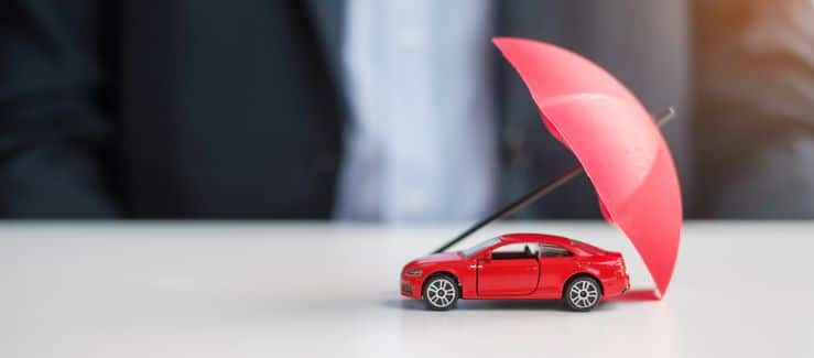 Red toy car on a white table with a small red umbrella. 