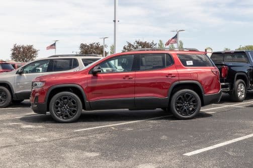 A red GMC Acadia SUV display at a car dealership.