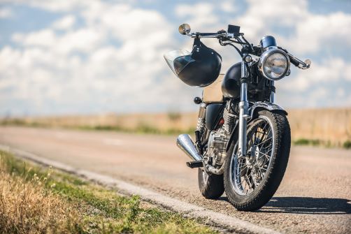 Motorcycle parked on the side of a road with a helmet handing from its handlebars.