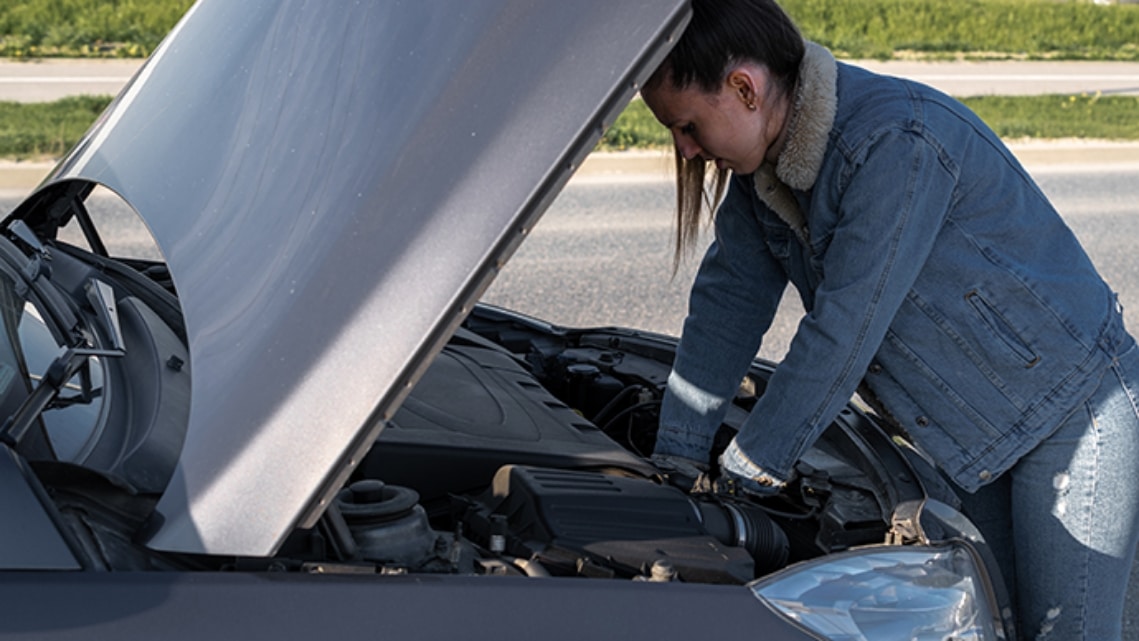 Woman fixing her car on the side of the road.